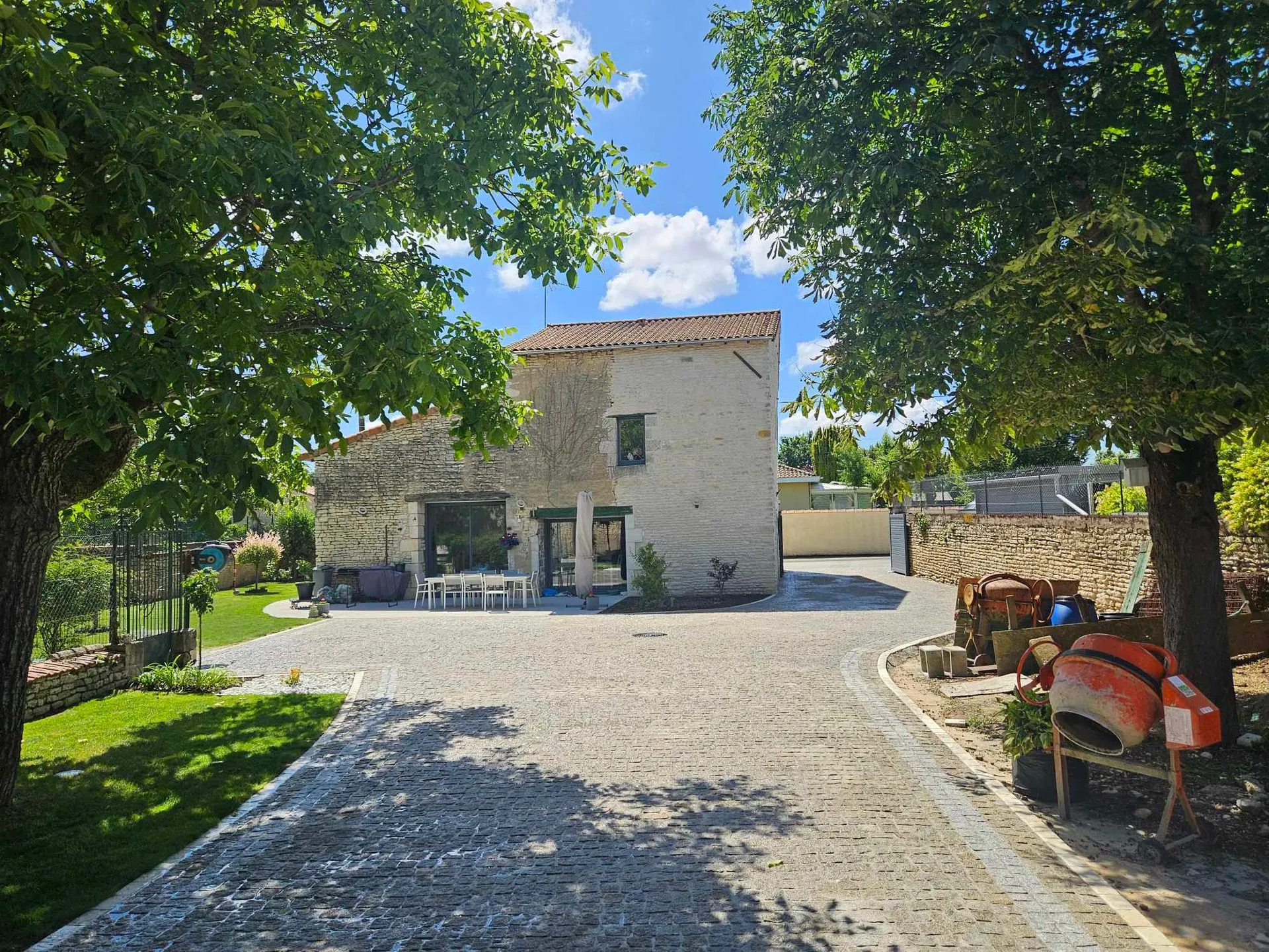 Grande cour en pavé granit doré devant une maison de caractère en pierre