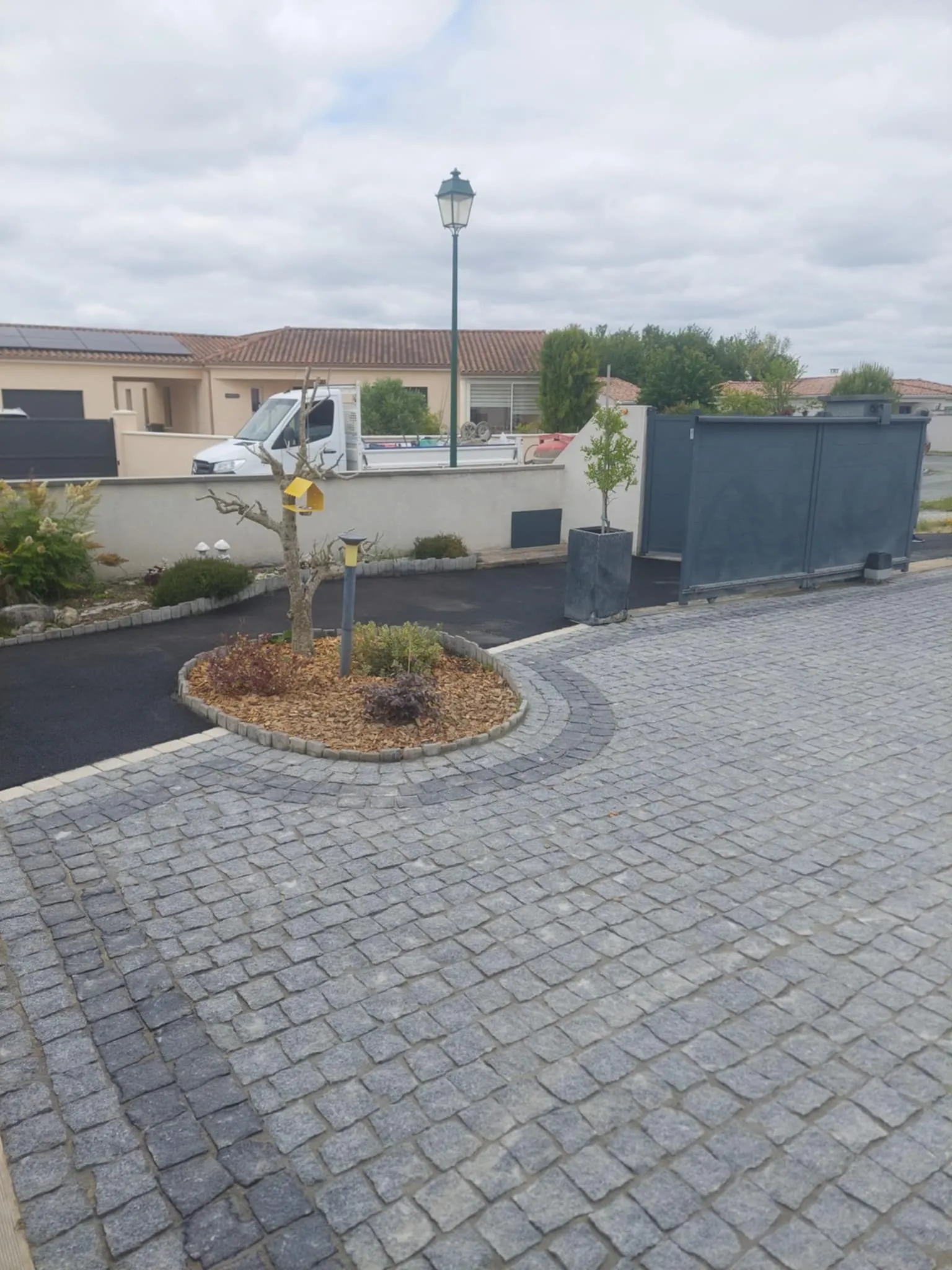 Cour en pavé granit gris avec massif paysager rond et lampadaire